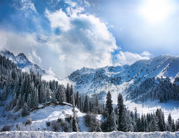 دره کوه‌های برفی زمستانی با مه و آفتاب در چومبولاک آلماتی قزاقستان