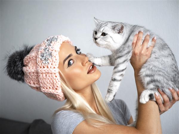 دختر زیبای تمام خانه با کلاه صورتی و یک گربه بریتانیایی بسیار سکسی و گرم به نظر می رسد آن زمستان را با گل ها بسیار گرم احساس کنید