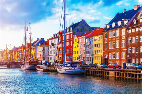 منظره زیبای غروب آفتاب تابستان از اسکله نیهاون با ساختمان‌های رنگی کشتی‌ها قایق‌های تفریحی و قایق‌های دیگر در شهر قدیمی کپنهاگ دانمارک