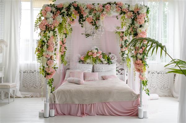 سوئیت ماه عسل با تخت سایبان فضای آزاد تخت سایبان چوبی مجلل با گل و بالش روی آن اتاق خواب زن در رنگ های صورتی و سفید فضای کپی تخت بزرگ راحت در اتاق خواب شیک