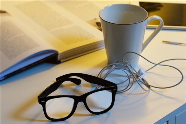 اشیاء مختلف روی میز - فنجان نوشیدنی گرم عینک کتاب و گوشی