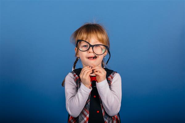 دختر بچه بامزه ای که با عینک با کت و شلوار مشکی روی پس زمینه آبی با فضای کپی خالی ژست گریم می زند بازگشت به موضوع مدرسه