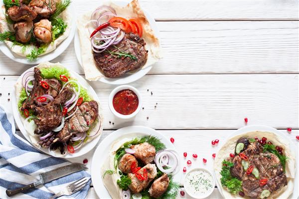 غذاهای گوشتی کبابی روی میز دراز نمای بالا در مجموعه ای از تنقلات bbq خوشمزه فضای آزاد در زمینه چوبی سفید منوی رستوران بوفه مفهوم ناهار