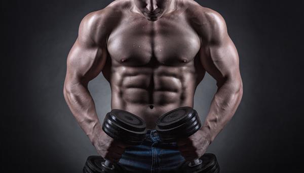 مرد بدنساز عضلانی متناسب با دمبل در پس زمینه تیره ورزش می کند