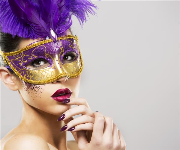 زن زیبا با مکاپ دراماتیک و رژ لب ارغوانی که ماسک ارغوانی به تن دارد پس زمینه روشن طلایی