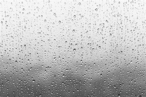 قطرات باران روی سطح شیشه های پنجره با پس زمینه ابری الگوی طبیعی قطرات باران جدا شده در پس زمینه ابری