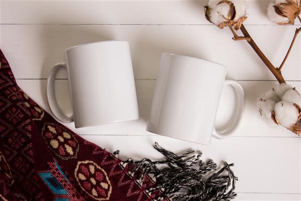 دو لیوان سفید یک جفت فنجان موکاپ فضای دنج زمینه چوبی تزیینات پنبه ای و پشمی برای هدایای زمستانی