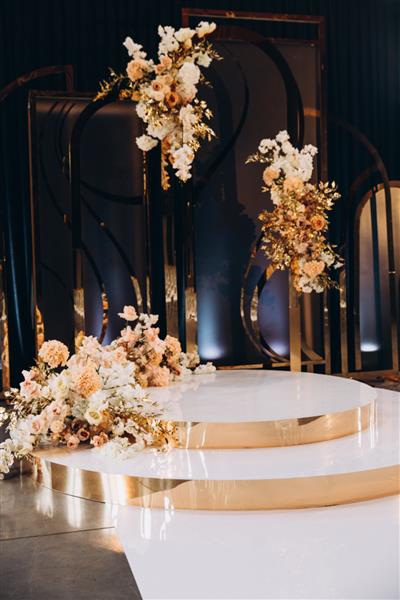 عروسی دکور محوطه مراسم به شکل یک تریبون با ترکیبات گل و شاخه های طلایی تزئین شده است