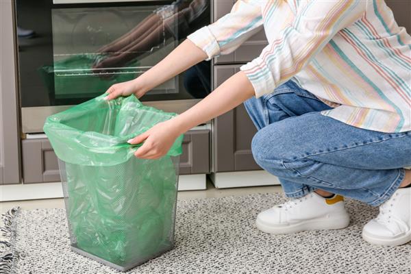 زن در حال گذاشتن کیسه زباله در سطل زباله در آشپزخانه