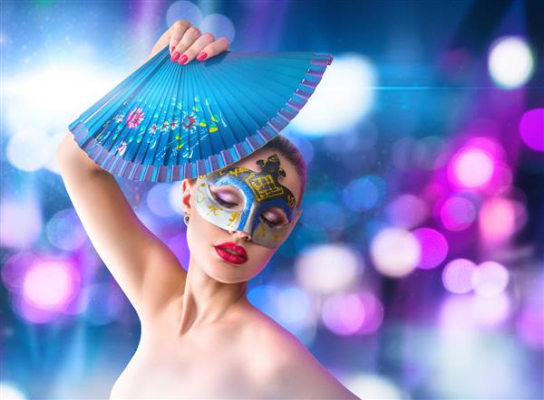 زن جوان زیبا با ماسک آبی کارناوال مرموز ونیزی در مقابل روشنایی شهر شبانه