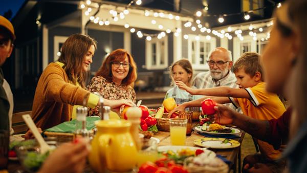 گروهی از افراد مختلف چند قومیتی که در حال تفریح ارتباط با یکدیگر و صرف شام در فضای باز هستند خانواده و دوستان در یک عصر گرم تابستانی بیرون از خانه خود جمع شدند