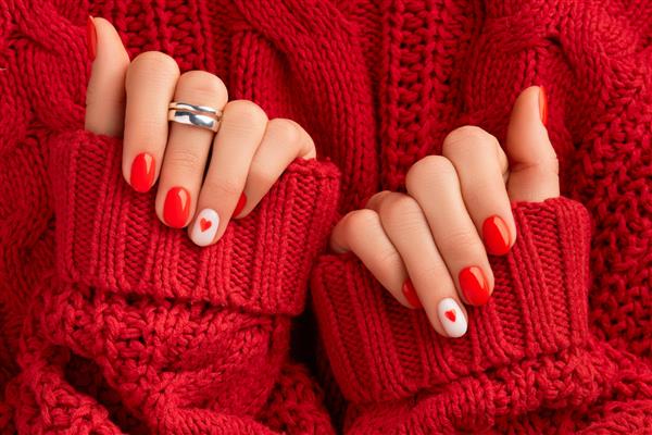 دست های زنانه مانیکور شده در ژاکت پشمی گرم قرمز طراحی ناخن شیک روز ولنتاین