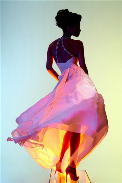 خانم جوان زیبا با لباسی شیک در یک استودیو عکس ژست گرفته است مدل سکسی در نورافکن های رنگی روشن پرتره زنی با لباس عروس سفید عکاسی هنری