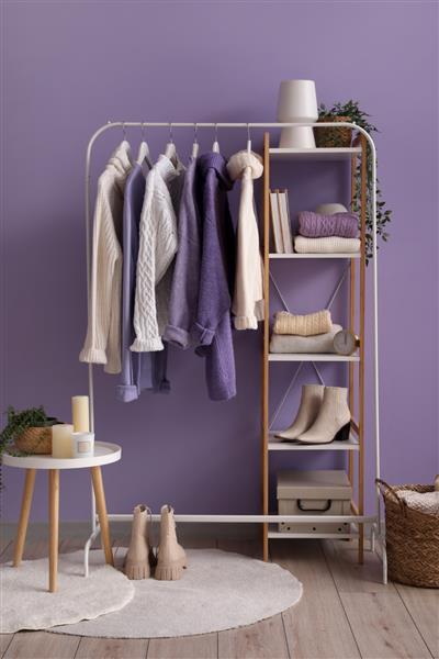 قفسه ای با ژاکت های بافتنی و قفسه بندی در نزدیکی دیوار رنگی در اتاق