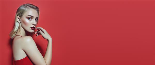 زن جوان زیبا با موهای بلوند در لباس قرمز در پس زمینه قرمز زنی با آرایش روشن و لب های قرمز بلوند در پس زمینه قرمز مفهوم تبلیغات برای لوازم آرایشی تزئینی