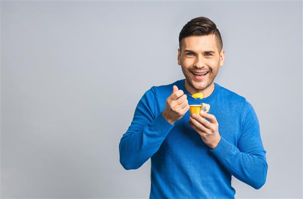 مرد جوان خوش‌تیپ اوکراینی خوشحال در حال خوردن ماست جدا شده روی پس‌زمینه سفید خاکستری مفهوم سبک زندگی سالم