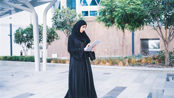 زن تاجر مسلمان عرب که در یک جلسه در فضای باز روی تبلت کار می کند بانوی تاجر عربستانی یا اماراتی با پوشیدن عبایا