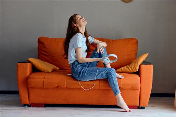 زن شاد روی مبل نارنجی در حال گوش دادن به موسیقی با هدفون سبک زندگی