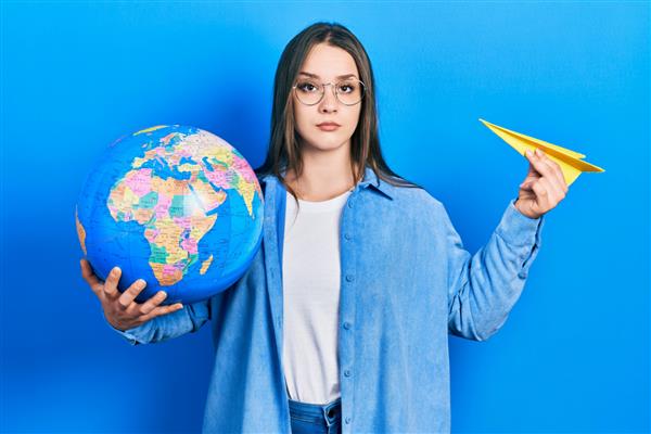 دختر جوان اسپانیایی تبار که هواپیمای کاغذی و توپ جهانی را در دست گرفته و با حالتی جدی در چهره آرام شده است نگاه ساده و طبیعی به دوربین