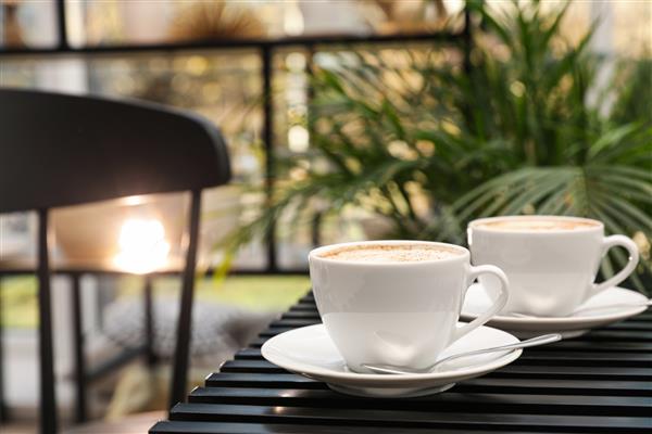 فنجان سرامیکی قهوه معطر با فوم روی میز چوبی در کافه
