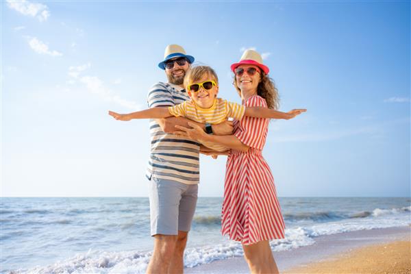 خانواده شاد در حال تفریح در ساحل مادر و پدر پسر را در پس زمینه آبی دریا و آسمان در آغوش گرفته اند مفهوم تعطیلات تابستانی
