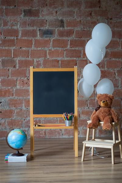 مفهوم بازگشت به مدرسه تخته گچی پشته کتاب کره زمین و خرس عروسکی روی پس زمینه دیوار آجری
