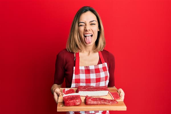 زن جوان بلوند قفقازی تخته به دست گرفته با گوشت خام که زبانش را بیرون آورده است خوشحال با بیان خنده‌دار