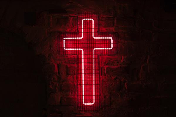 صلیب نئونی قرمز درخشان بر روی دیوار پشت میله ها در تاریکی آویزان است