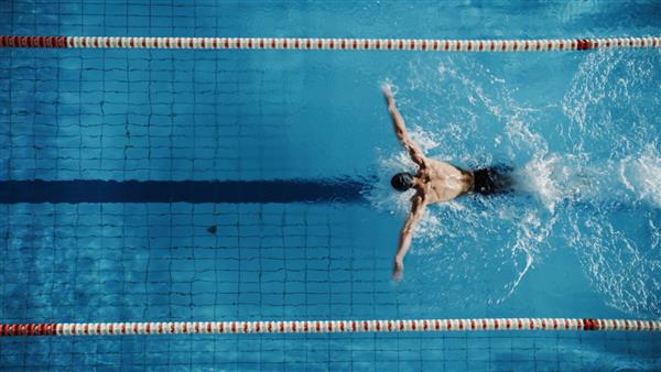 نمای بالای هوایی شناگر مرد در حال شنا در استخر آموزش حرفه ای ورزشکار تعیین شده برای قهرمانی با استفاده از تکنیک پروانه نمای بالا شات