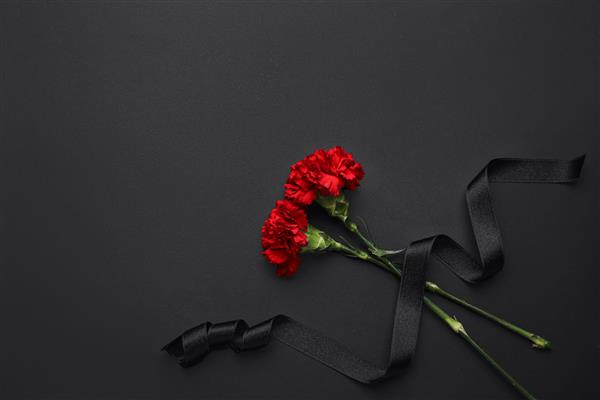روبان تشییع جنازه مشکی با گل های میخک در پس زمینه تیره