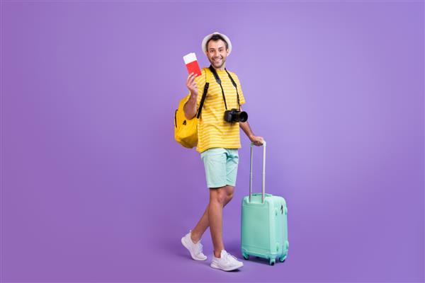 عکس کنار نمایه با اندازه کامل کیسه بلیط سفر به خارج از کشور لبخند مثبت پسر جوان جدا شده روی پس‌زمینه رنگ بنفش