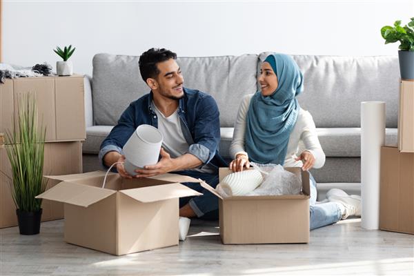 زن و شوهر خوش تیپ خانواده عرب با حجاب در حال باز کردن وسایل و گفتگو رویاپردازی در مورد آینده مرفه نقل مکان به آپارتمان جدید یا خرید خانه شخصی