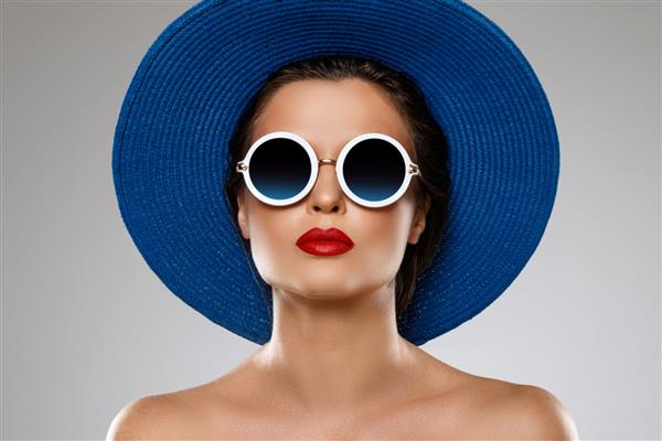 زن جوان و زیبا با کلاه آبی و عینک آفتابی برای تعطیلات آماده است