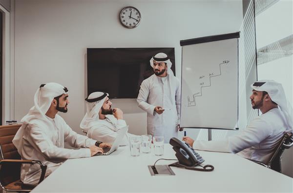 تصویر سینمایی یک گروه عربی از مردم که در دفتر کار می کنند چهار مرد با لباس‌های سنتی از دبی در حال ساخت برنامه‌های تجاری در داخل خانه