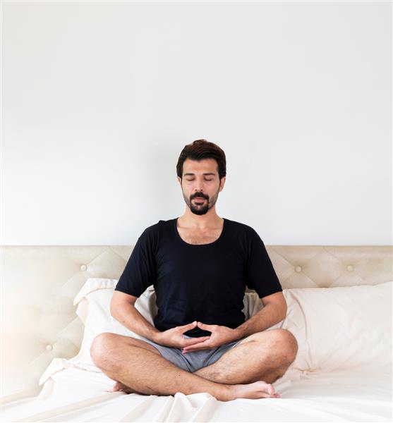 مردی با سبیل در حال مدیتیشن در حالی که صبح روی تخت نشسته است مرد جوان در حال انجام یوگا در رختخواب مرد در حال مدیتیشن روی تخت در خانه قبل از خواب روی تخت مدیتیشن کنید