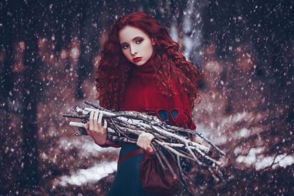 بازسازی تاریخی دختر روستایی زیبا با لباس سلتیک تاریخی در جنگل زمستانی چوب برس جمع می کند