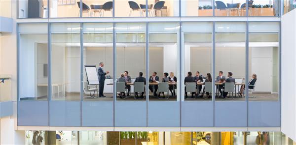 نمای گسترده ای از افراد تجاری که در یک اتاق کنفرانس جلسه دارند از دیوارهای شیشه ای خارج از یک ساختمان مدرن دیده می شود