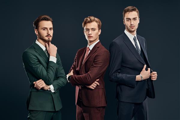 مد مردانه سه مرد خوش تیپ با کت و شلوارهای زیبا که با هم روی پس زمینه آبی تیره ژست گرفته اند زیبایی مردانه پرتره استودیویی