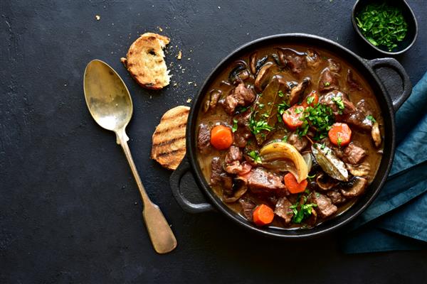 گوشت گاو بورگینیون - خورش گوشت با سبزیجات و قارچ با شراب قرمز در یک ماهیتابه روی تخته سنگ سیاه سنگ یا زمینه بتونی غذای سنتی غذاهای فرانسوی نمای بالا با فضای کپی