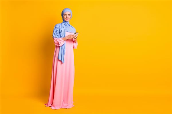 نمای سایز بدن تمام قد از یک مسلمان زیبا و زیبا با لباس حجاب با استفاده از وبلاگ دستگاه جدا شده در پس زمینه رنگ زرد روشن