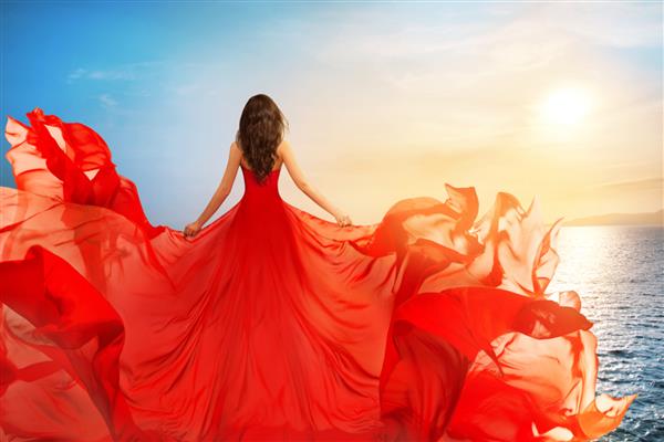 نمای عقب زنی با لباس پرنده قرمز که در باد بال می زند دختری با لباس تکان دهنده در دریای غروب آفتاب