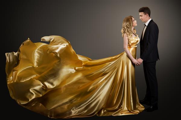 زن و شوهر زن زیبا با لباس ابریشمی طلایی و مرد شیک با کت و شلوار لباس مجلسی که در باد بال می زند