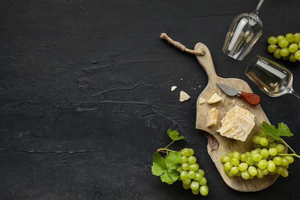 دو لیوان شراب سفید و یک بشقاب پنیری خوشمزه با میوه روی بشقاب آشپزخانه چوبی در زمینه سنگ سیاه نمای بالا فضای کپی غذا و نوشیدنی لذیذ