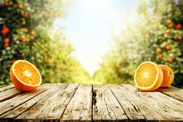 پس زمینه میز فضای آزاد برای دکوراسیون شما میوه های نارنجی تازه و چشم انداز تابستانی باغ با درختان و نور خورشید زمان تابستان