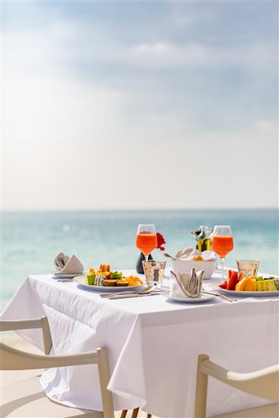 غذای لوکس صبحانه روی میز سفید با پس زمینه زیبای دریای استوایی تعطیلات تابستانی صبحگاهی و مفهوم تعطیلات رمانتیک سفرهای لوکس و سبک زندگی