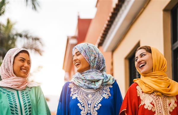 زنان مسلمان شادی که در مرکز شهر قدم می زنند - دختران جوان عرب در حال تفریح و گذراندن وقت و خندیدن با هم در فضای باز - مفهوم مردم فرهنگ و مذهب