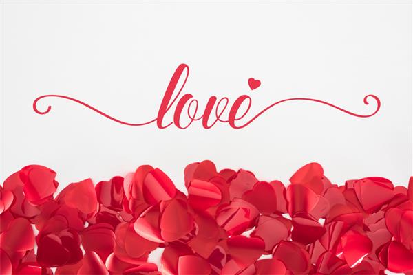 نمای نزدیک از گلبرگ های زیبای قلبی شکل قرمز در پس زمینه خاکستری با حروف عشق مفهوم روز ولنتاین