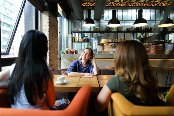 زنان جوانی که در کافه دنج نشسته اند لبخند می زنند و قهوه می نوشند مفهوم دوستی و زندگی شهری