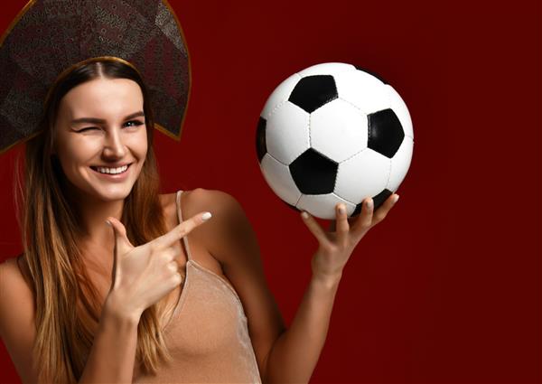 بازیکن زن ورزشکار هوادار به سبک روسی با کلاه کوکوشنیک توپ فوتبال را در دست گرفته و با خنداندن شاد با فضای کپی متن آزاد جدا شده روی پس‌زمینه سفید جشن می‌گیرد