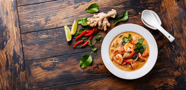 سوپ تایلندی تند تام یام کونگ با میگو غذاهای دریایی شیر نارگیل و فلفل چیلی در کاسه ای روی فضای کپی پس زمینه چوبی